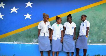 Four students stand in front of a mural of the flag of Solomon Islands.
