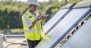 A woman in a hard hat writes in a notebook next to a solar panel