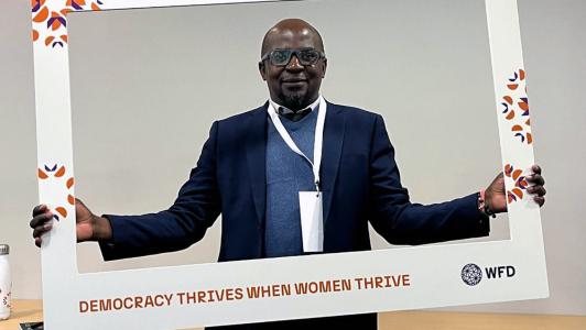 Viwemi Chavula in cut out sign reading democracy thrives when women thrive